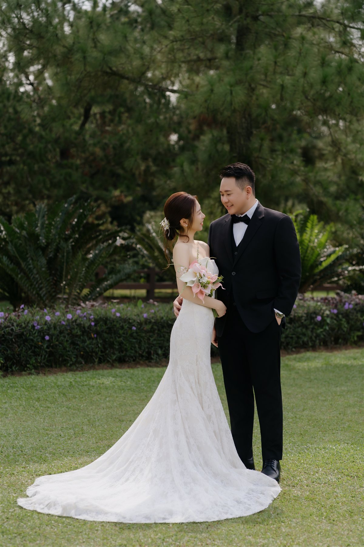 Steven and Charis smiling at each other in a garden, her bouquet in hand